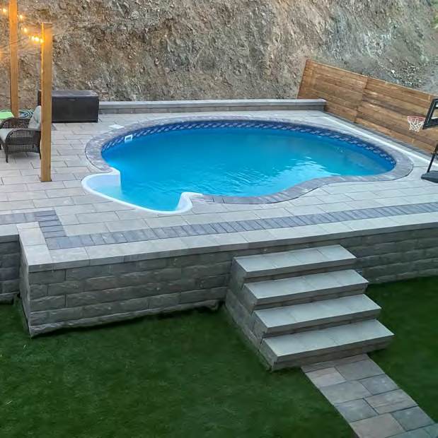 Kidney shaped pool with block retaining wall and steps down to the lawn